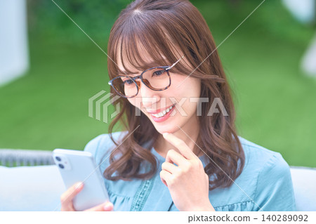 一位戴著眼鏡的年輕女子在戶外,一邊看著智慧型手機一邊思考。 一位戴著眼鏡的年輕女子在戶外,一邊看著智慧型手機一邊思考。 140289092