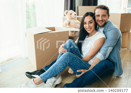 Happy Couple hugging and sitting on floor into their new home with many carton boxes on background 140289177