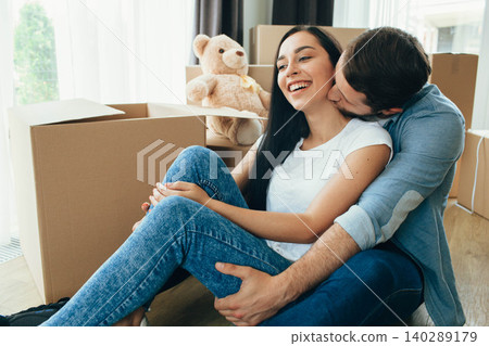 lovely man kissing his wife while sitting on floor at new home. Happy couple moving home, beginning new life to new apartment 140289179