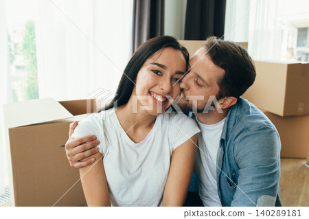 Mixed race couple happy moving at new home. Man and woman hugging and sitting on floor near cardboard boxes Mixed race couple happy moving at new home. Man and woman hugging and sitting on floor near cardboard boxes 140289181