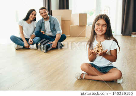 happy girl holding toy house, after her sitting happy parents into their new house. Moving new apartment 140289190
