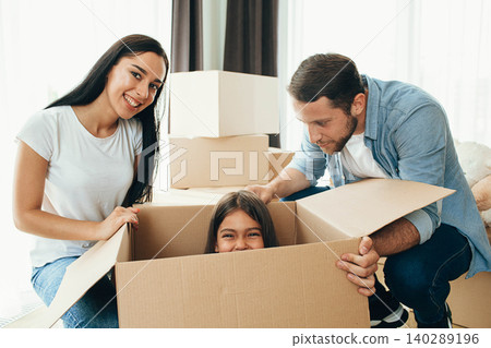 Happy family having fun while moving into new apartment. Mother, father and daughter together smiling, with Cardboard boxes on background Happy family having fun while moving into new apartment. Mother, father and daughter together smiling, with Cardboard boxes on background 140289196