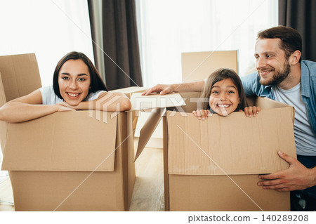 Happy family having fun with Cardboard boxes while moving into new apartment. Mother, father and daughter together smiling, happy young family Happy family having fun with Cardboard boxes while moving into new apartment. Mother, father and daughter together smiling, happy young family 140289208
