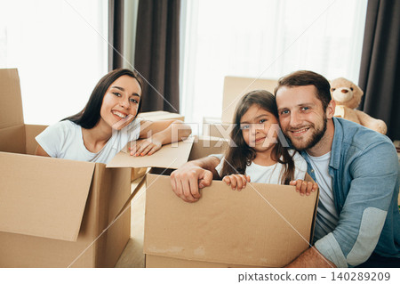 Happy family having fun while moving into new apartment. Mother, father and daughter together smiling, with Cardboard boxes on background Happy family having fun while moving into new apartment. Mother, father and daughter together smiling, with Cardboard boxes on background 140289209