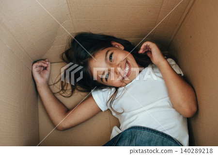 little girl playing inside a cardboard box, into her new house. little girl playing inside a cardboard box, into her new house. 140289218