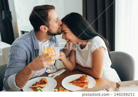 Happy couple kissing and have dinner with pizza at home. Its a good time spending home Happy couple kissing and have dinner with pizza at home. Its a good time spending home 140289251