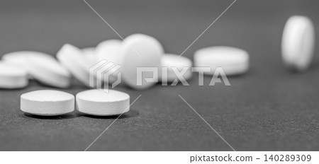 White round medical pills scattered on a dark slate surface White round medical pills scattered on a dark slate surface 140289309