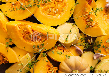 The scene shows various pieces of cut squash placed on a wooden table. Fresh thyme sprigs are scattered among the squash. Natural light fills the area, emphasizing the colors The scene shows various pieces of cut squash placed on a wooden table. Fresh thyme sprigs are scattered among the squash. Natural light fills the area, emphasizing the colors 140289324