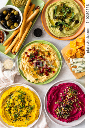 A vibrant spread showcases different types of hummus including classic, beetroot, broccoli, and turmeric. Accompanied by olives and breadsticks, it invites sharing and enjoyment A vibrant spread showcases different types of hummus including classic, beetroot, broccoli, and turmeric. Accompanied by olives and breadsticks, it invites sharing and enjoyment 140289338