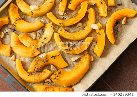 Butternut squash slices are arranged on a tray with herbs and garlic, ready for roasting. This is part of a cooking process in a kitchen setting Butternut squash slices are arranged on a tray with herbs and garlic, ready for roasting. This is part of a cooking process in a kitchen setting 140289341
