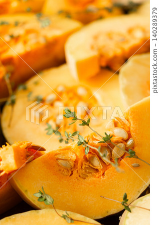Slices of yellow squash are laid out on a wooden surface. Fresh thyme sprigs are placed on the squash. This scene shows preparation for cooking a meal or dish Slices of yellow squash are laid out on a wooden surface. Fresh thyme sprigs are placed on the squash. This scene shows preparation for cooking a meal or dish 140289379