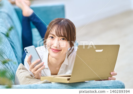 A young woman on a sofa, holding her smartphone and smiling at the camera. A young woman on a sofa, holding her smartphone and smiling at the camera. 140289394