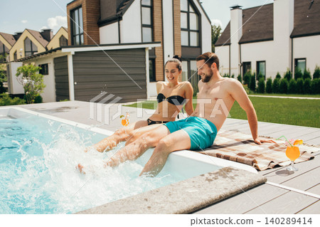 Lovely heteroseksual couple having water resting. Man and woman sitting near water pool and funny splashing water their legs Lovely heteroseksual couple having water resting. Man and woman sitting near water pool and funny splashing water their legs 140289414