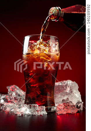 Sparkling cola is poured from a bottle into a misted glass with ice. Sparkling cola is poured from a bottle into a misted glass with ice. 140289592