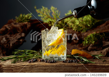 Gin is poured from the bottle into a glass with ice and a lemon wedge. Gin is poured from the bottle into a glass with ice and a lemon wedge. 140289609
