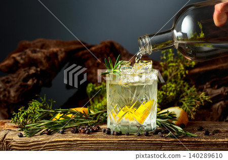 Gin is poured from the bottle into a glass with ice and a lemon wedge. Gin is poured from the bottle into a glass with ice and a lemon wedge. 140289610