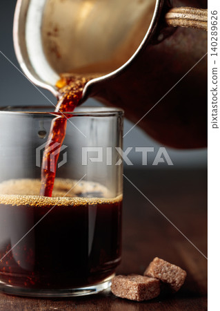 Black coffee is poured into a glass cup. Black coffee is poured into a glass cup. 140289626