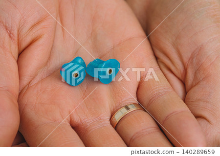 Earplugs for use in an airplane at high atmospheric pressure with pressure valve in hands, top view. Personally molded earplugs Earplugs for use in an airplane at high atmospheric pressure with pressure valve in hands, top view. Personally molded earplugs 140289659