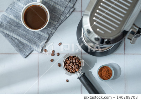 A flat lay of a cup of black coffee, a portafilter with roasted beans and an espresso machine 140289708