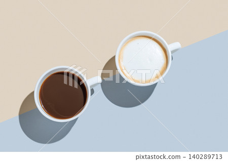 Two white cups of freshly brewed espresso and cappuccino on a yellow and blue background Two white cups of freshly brewed espresso and cappuccino on a yellow and blue background 140289713