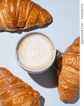Flat lay of cappuccino coffee cup and fresh croissants on blue background with shadow. Flat lay of cappuccino coffee cup and fresh croissants on blue background with shadow. 140289732