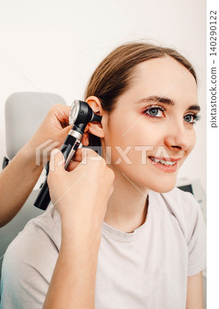 Hearing exam for a woman. Diagnosis of disorders and hearing testing in adults. Female patient examining an ear with an otoscope Hearing exam for a woman. Diagnosis of disorders and hearing testing in adults. Female patient examining an ear with an otoscope 140290122