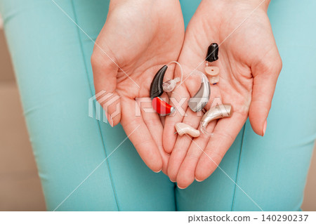 Different types of hearing aids in female hands, top view. Hearing solution, very stylish BTE and intra-ear hearing aids in different colors Different types of hearing aids in female hands, top view. Hearing solution, very stylish BTE and intra-ear hearing aids in different colors 140290237