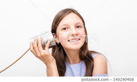 Smiling girl with a tin can telephone near the ear, playing in retro connected chat. Child isolated on white background Smiling girl with a tin can telephone near the ear, playing in retro connected chat. Child isolated on white background 140290408
