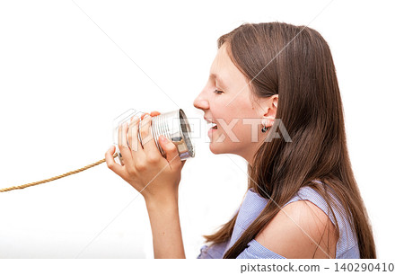 Beautiful teenage girl saying in a tin can telephone. Children's retro phone - wire tin can, chat that connected people for talking, hearing solutions Beautiful teenage girl saying in a tin can telephone. Children's retro phone - wire tin can, chat that connected people for talking, hearing solutions 140290410