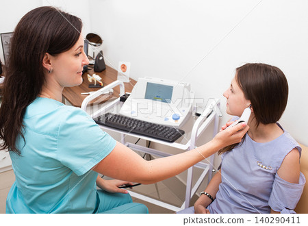 Audiologist doing a hearing exam on a girl. Impedance audiometry. Methods for testing the middle ear in a child Audiologist doing a hearing exam on a girl. Impedance audiometry. Methods for testing the middle ear in a child 140290411