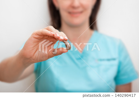 Hearing aids, deafness treatment. Close-up of audiologist's hand holding modern hearing aid 140290417