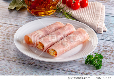 Ham rolls with savory filling on white plate with herbs and tomatoes 140290456
