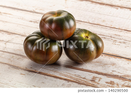Three dark purple green heirloom tomatoes on rustic wooden table Three dark purple green heirloom tomatoes on rustic wooden table 140290500