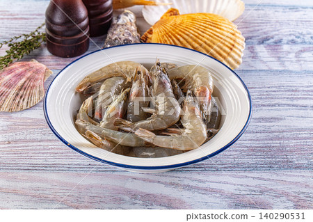 Raw shrimp in white bowl with blue rim on rustic wooden table with seashells and herbs Raw shrimp in white bowl with blue rim on rustic wooden table with seashells and herbs 140290531