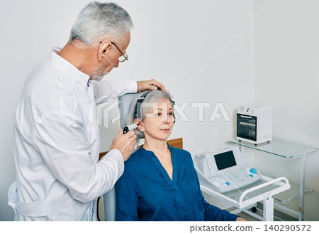 Mature audiologist with tympanometer probe doing procedure tympanometry or impedance audiometry for senior woman patient at hearing clinic 140290572