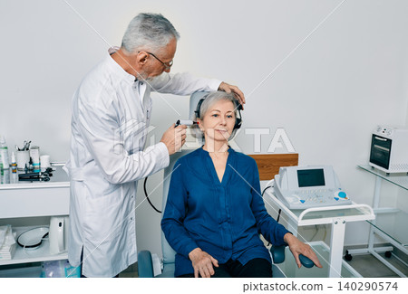 Senior woman while tympanometry or impedance audiometry and test of middle-ear function with ENT-doctor using tympanometer probe at hearing center Senior woman while tympanometry or impedance audiometry and test of middle-ear function with ENT-doctor using tympanometer probe at hearing center 140290574
