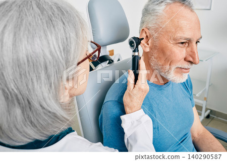 Otolaryngologist doctor checking senior man's ear using otoscope or auriscope at hearing center. Audiology Otolaryngologist doctor checking senior man's ear using otoscope or auriscope at hearing center. Audiology 140290587