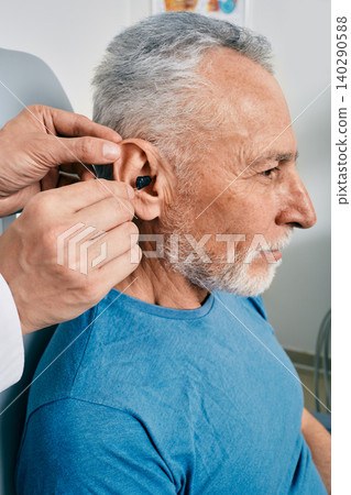 Senior man while installation hearing aid into his ear by his audiologist, close-up. Hearing treatment for hearing impaired people 140290588
