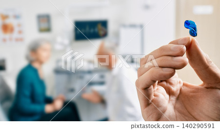 Intra-ear hearing aid in doctor hands, close-up. Selection of hearing aids for senior female patient with audiologist over background, soft focus 140290591