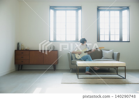 A young man playing the guitar on a sofa. A young man playing the guitar on a sofa. 140290748