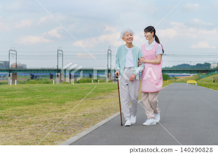 A Japanese senior woman and a young female caregiver strolling along the riverbank. A Japanese senior woman and a young female caregiver strolling along the riverbank. 140290828