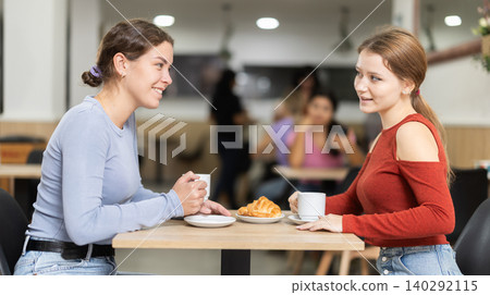 Two young girls talking over coffee and croissant in cafeteria Two young girls talking over coffee and croissant in cafeteria 140292115