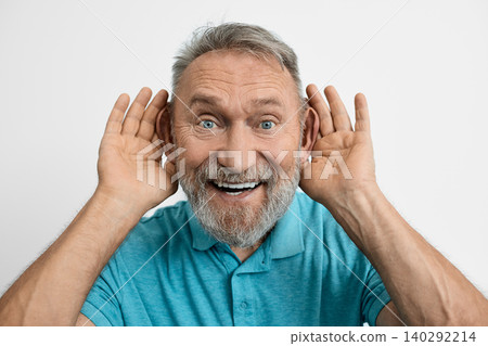 Funny elderly man with toothy smile having fun and holding hands near his ears and asking what did you say .Hearing problems 140292214