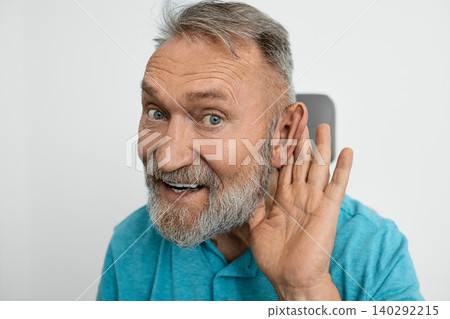 Old man with hearing problems in hearing clinic, hearing impaired and holding hand near ear to hear better Old man with hearing problems in hearing clinic, hearing impaired and holding hand near ear to hear better 140292215