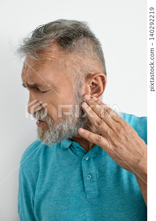 Senior man struggling with hearing aspects, gently touching his ear as discomfort shows on his face Senior man struggling with hearing aspects, gently touching his ear as discomfort shows on his face 140292219