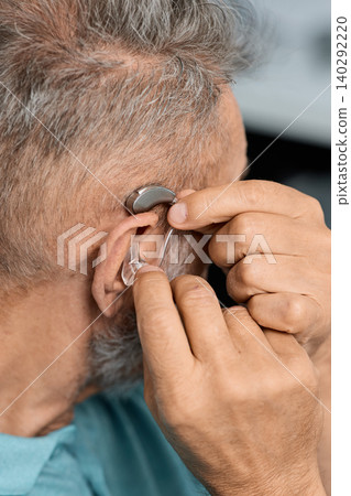 Grey-haired senior man with hearing impairment using hearing aid. Hearing solutions for deafness people 140292220