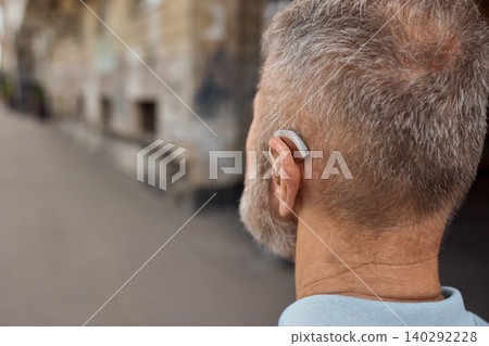 Human life with a hearing aid. Senior man with a hearing aid behind the ear in a noisy city hears people around well Human life with a hearing aid. Senior man with a hearing aid behind the ear in a noisy city hears people around well 140292228