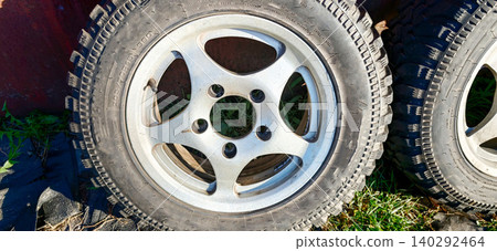 Silver alloy wheel with five spokes and black tire resting on grass beside another tire, showcasing detailed design and texture in natural outdoor setting 140292464
