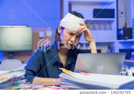 Injured young Asian office worker wearing head bandage while working on laptop in office, health and work pressure concept. Injured young Asian office worker wearing head bandage while working on laptop in office, health and work pressure concept. 140292795