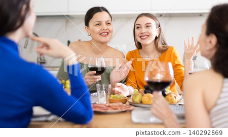 Cheerful besties drinking wine and chatting during home gathering 140292869